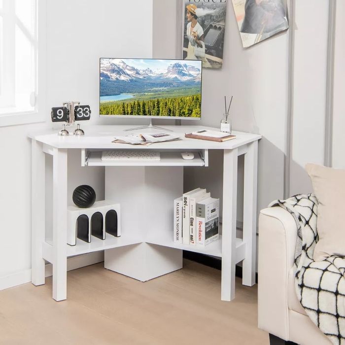 A white corner desk complete with a computer, keyboard, clock, decorative items, and books.