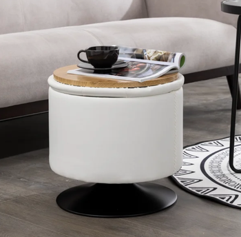 A white storage ottoman with its lid flipped to reveal the wooden tray side, adorned with a magazine and a coffee mug.