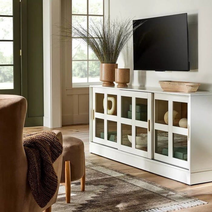 A white TV stand featuring various decorative items placed underneath a flat-screen TV.