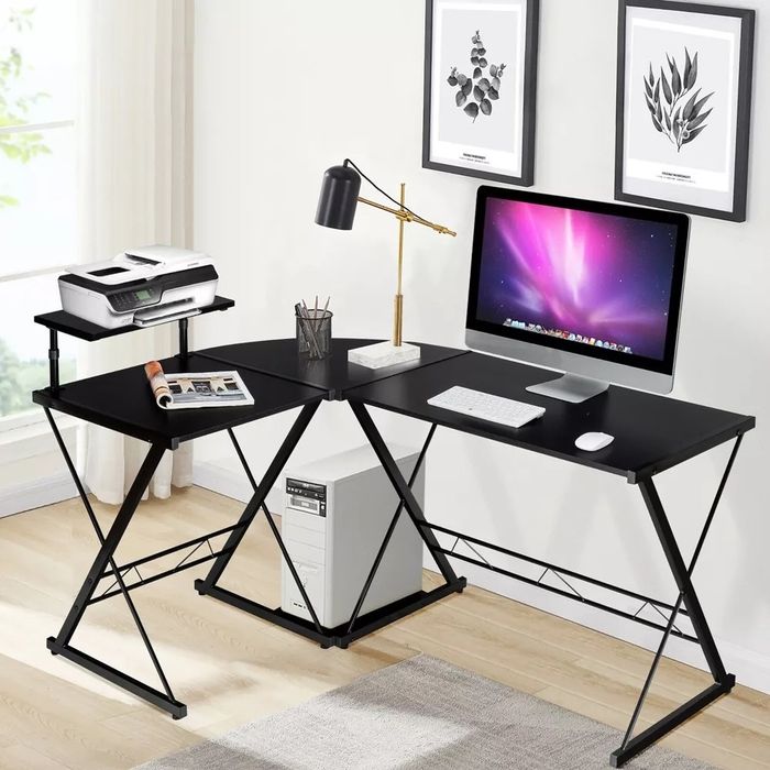 The black L-shaped desk with a computer, printer, and desk lamp placed on it.