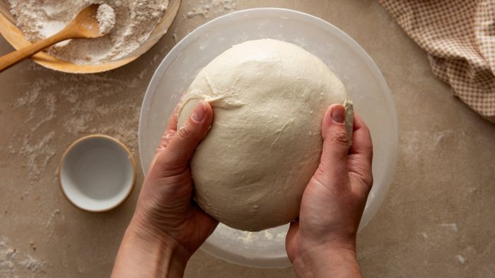 A pair of hands lifting a ball of bread dough above a bowl.