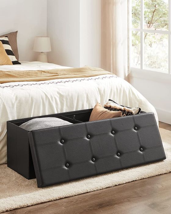 A black rectangular storage ottoman bench with the lid removed and pillows neatly packed inside