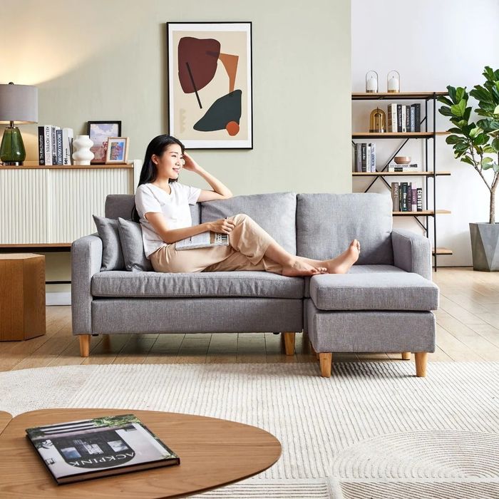 A model relaxing on a light gray linen sectional sofa.