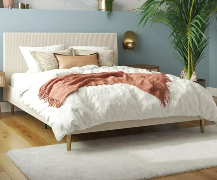 A queen-sized bed with a beige headboard and frame, complete with cozy blankets — an ideal setup for a minimalist yet comfortable bedroom.