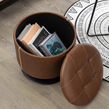 A brown storage ottoman with the lid removed, showing books neatly stored inside.