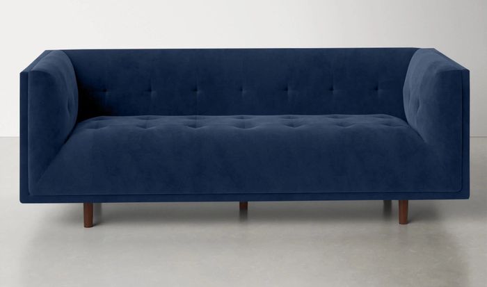 a sapphire velvet tufted sofa with brown wooden legs, elegantly upholstered