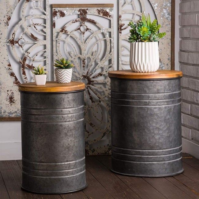 Two metal stools with a vintage milk canister aesthetic, each showing unique wear with dents and discoloration. The lids feature a smooth, natural wood finish.