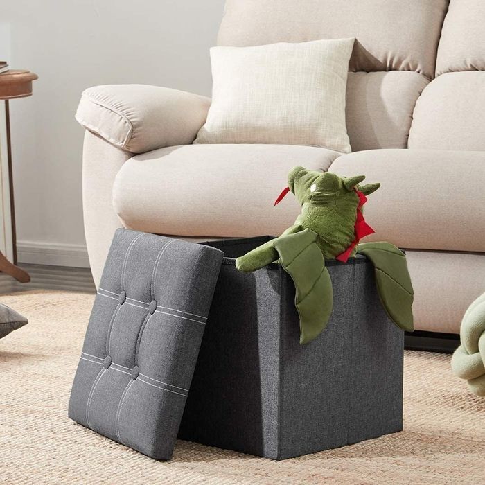 The grey cube-shaped storage ottoman with the lid removed, showing items neatly stored inside