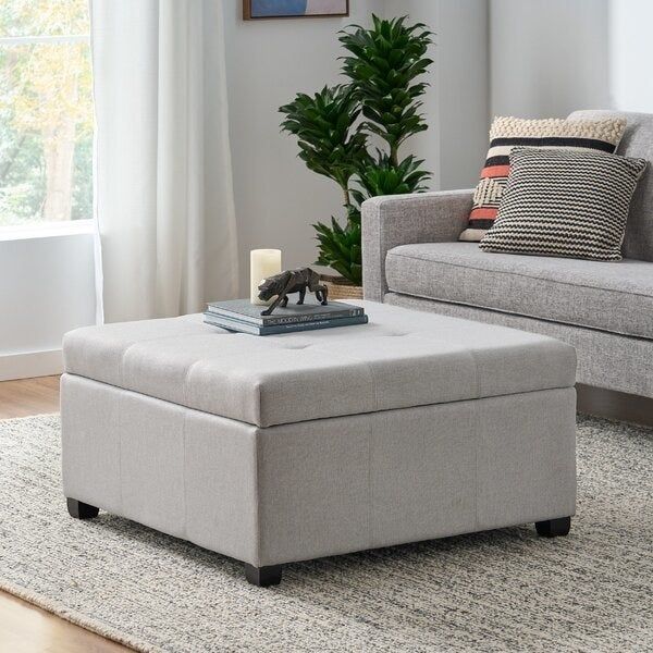 A large grey storage ottoman with books and decorative items placed on top, positioned in front of a couch.