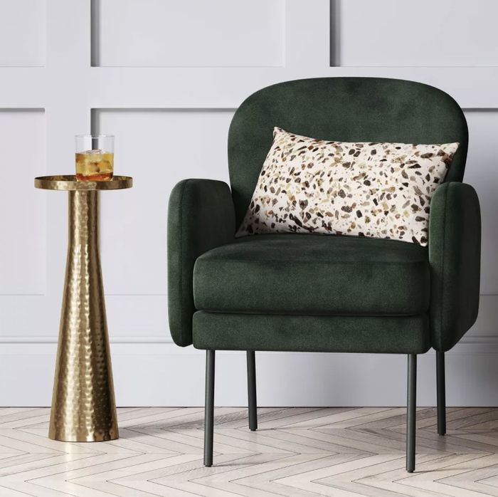 A gold side table, complete with a cocktail placed next to a cozy accent chair