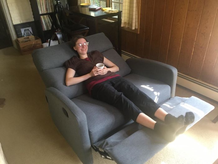 A person relaxes on a recliner, smiling and holding a drink, in a warm and inviting living room