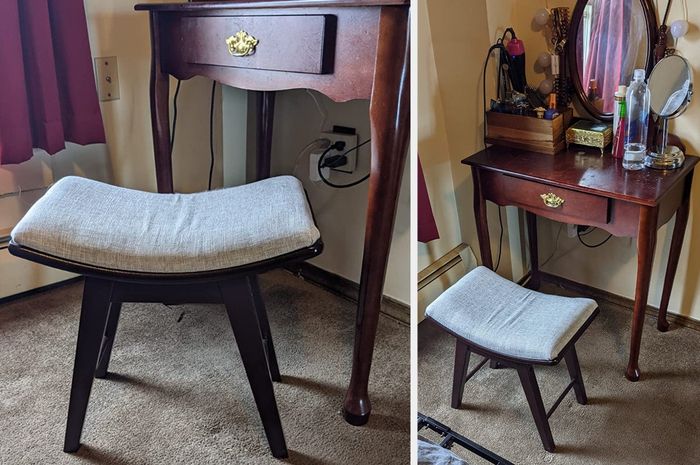 A reviewer’s image of a curved stool with dark brown wooden legs and a gray fabric seat, positioned in front of a wooden vanity.