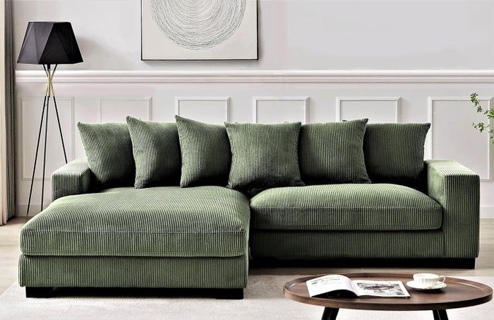A green L-shaped sofa with comfy cushions in a living room, paired with a coffee table featuring a magazine on top.