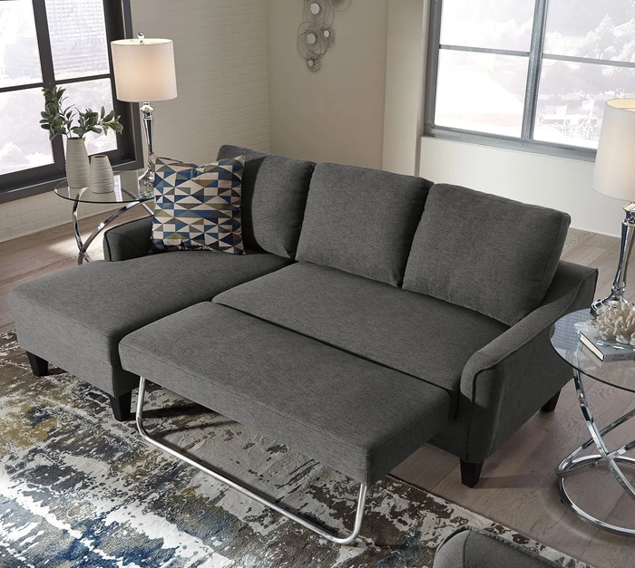 Grey sectional sofa with a pull-out bed, positioned in a modern living room featuring lamps and a geometric-patterned pillow.
