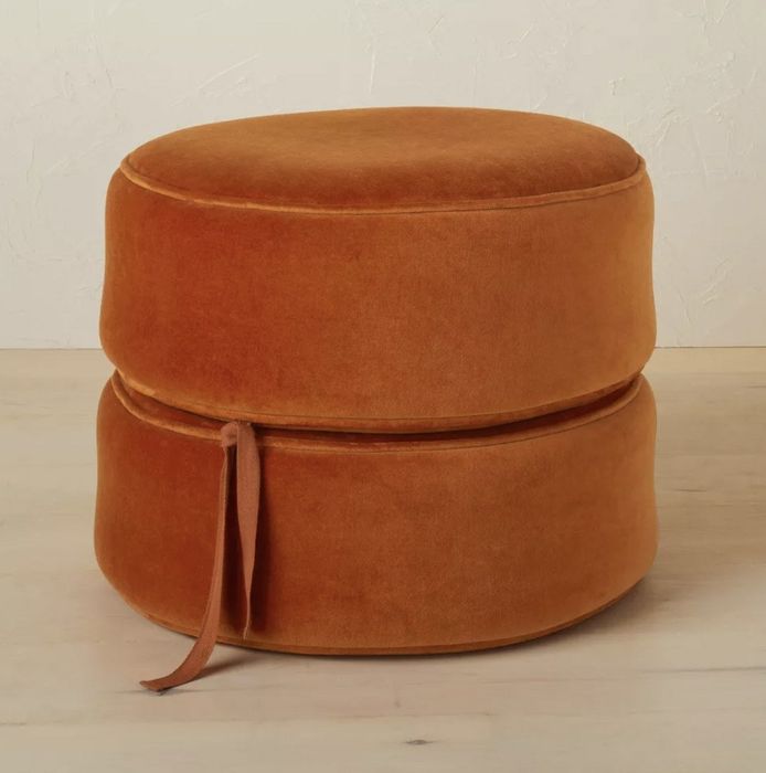 The round pouf in a warm rust color, with the cushions neatly stacked on top of each other.