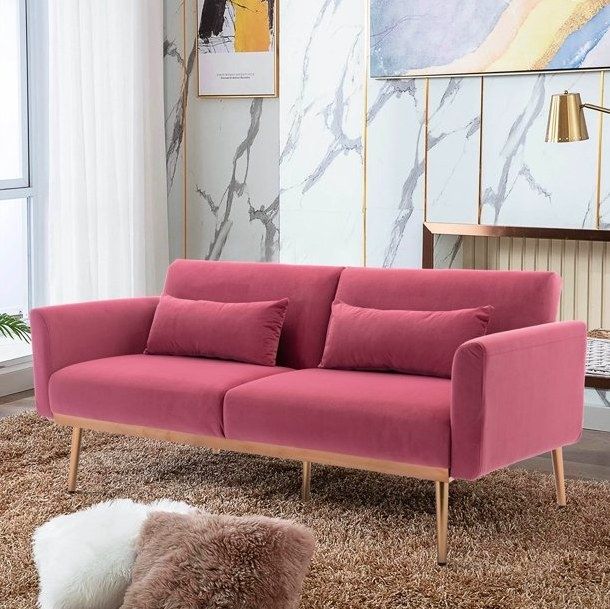 A pink velvet couch positioned in a cozy living room atop a soft brown fluffy rug.