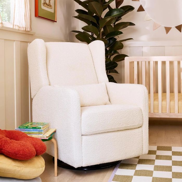 A contemporary nursery featuring a plush white armchair, a wooden crib, a tiny table adorned with kids' books, a paw-shaped cushion, and a vibrant green houseplant