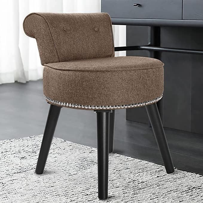 A brown fabric vanity chair with a short back, black wooden legs, and silver studs along the bottom, resting atop a soft carpet.