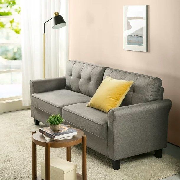 A gray sofa with a yellow pillow and a wooden side table positioned beside it creates a stylish and cozy setup.