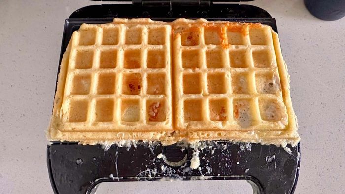 Waffle cooking in a waffle iron with uneven, messy edges.