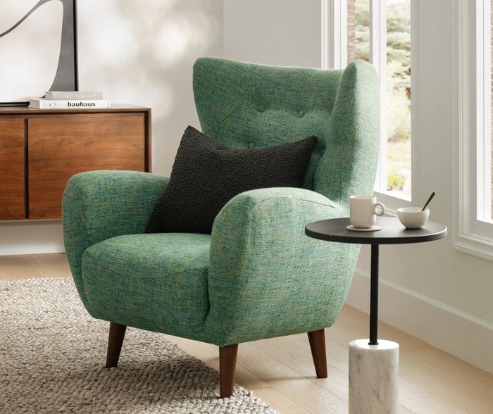 A textured armchair with rounded arms, placed beside a side table holding a tea set in a bright and inviting room