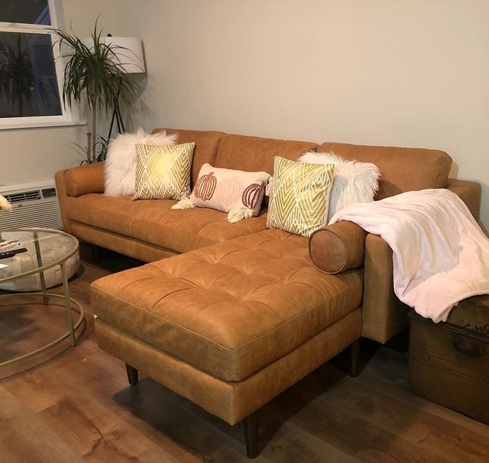 A tan leather sectional adorned with decorative cushions and a cozy throw blanket, all set in a warm living room environment.