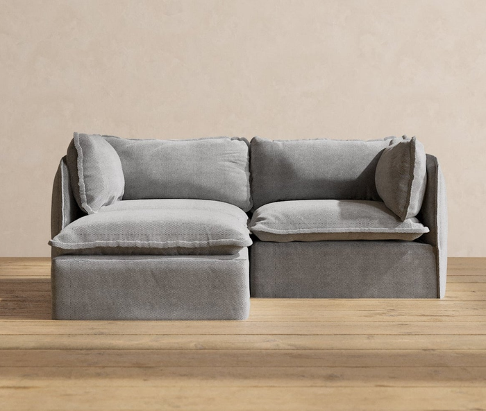 A modern gray sectional sofa with soft cushions on a wooden floor in a minimalist living room.