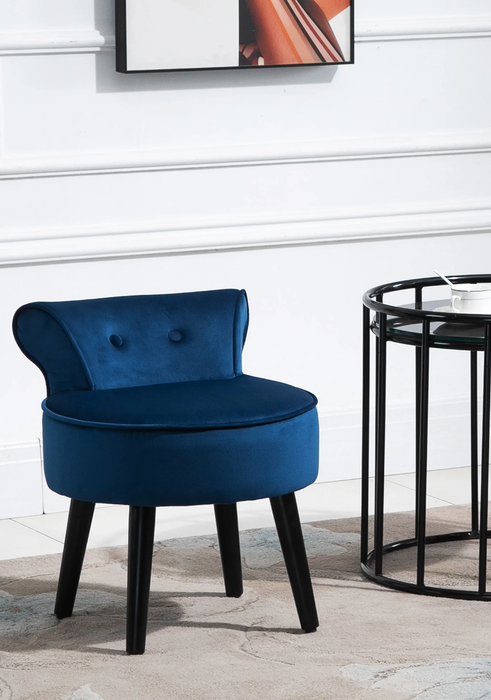 A dark blue velvet vanity stool with black wooden legs and a tufted backrest, sitting next to a sleek black metal side table.