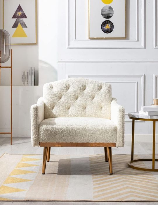 A comfortable upholstered armchair featuring wooden legs, placed in a contemporary living room adorned with abstract framed artwork on the walls