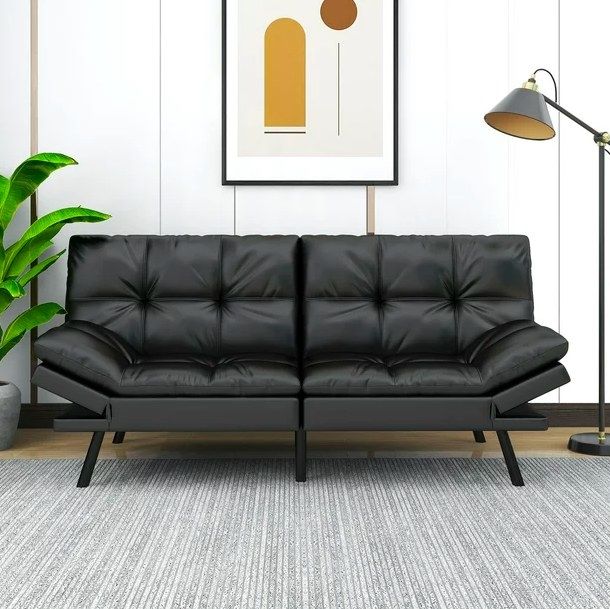 A black futon with a floor lamp beside it and a piece of artwork hanging above, adding a chic touch to any space.