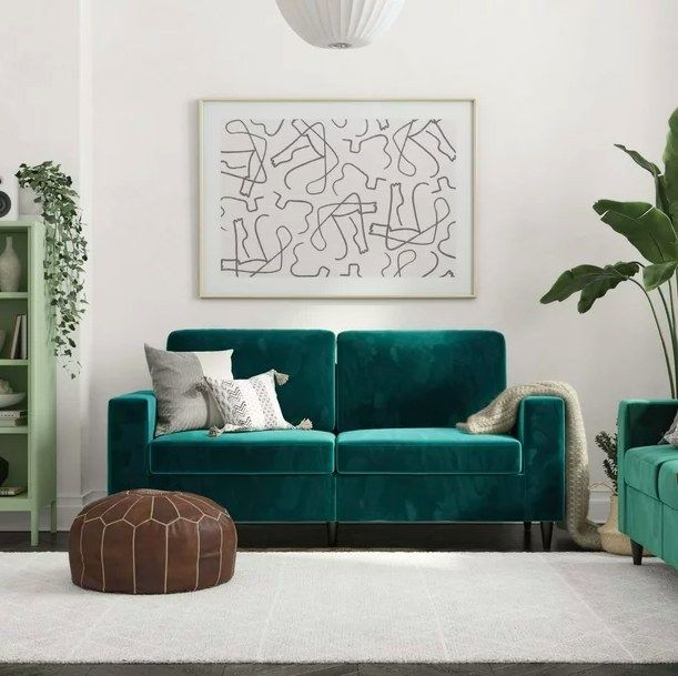 A green velvet sofa complete with throw pillows, a cozy blanket, and a chic leather pouf resting beside it.