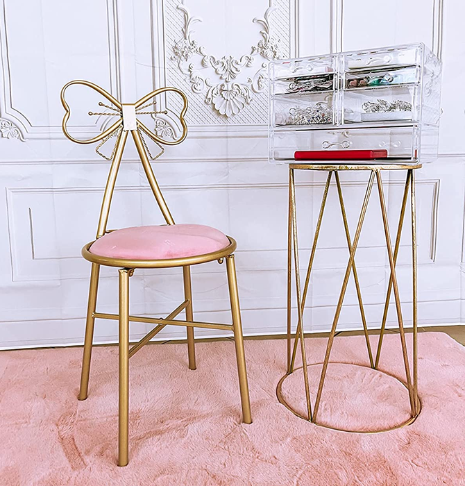 Reviewer image showing a gold metal vanity chair with a bow-shaped backrest, paired with a pink velvet seat and a matching gold side table topped with jewelry.