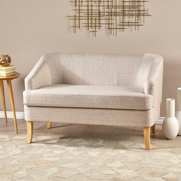A beige loveseat positioned beside two white vases and a wooden side table, creating a serene and balanced design.