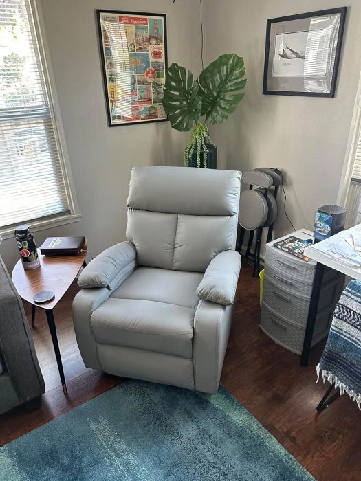 A contemporary living room featuring a plush leather recliner, a wooden side table, a framed poster on the wall, and a large indoor plant