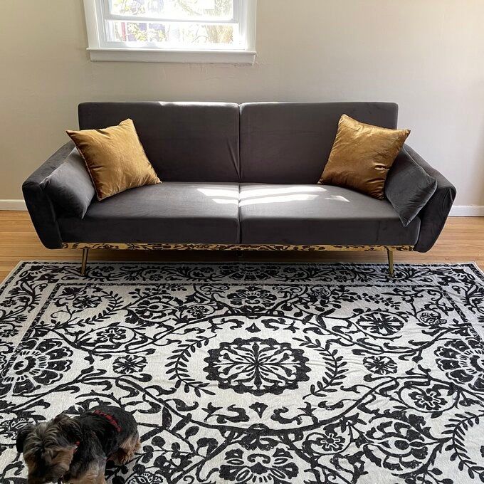 A gray velvet futon adorned with two yellow throw pillows.
