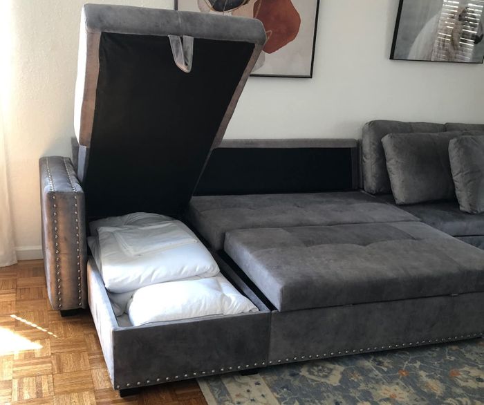 A reviewer's photo showing the couch in gray, fully extended into a sleeper with the storage compartment visible.