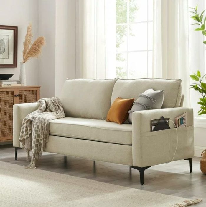 A cream-colored sofa featuring side pockets, throw pillows, and a cozy blanket resting on it.