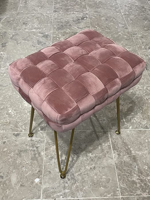 A reviewer’s image of a pink velvet vanity stool with a woven design and gold curved legs placed on a tiled floor.