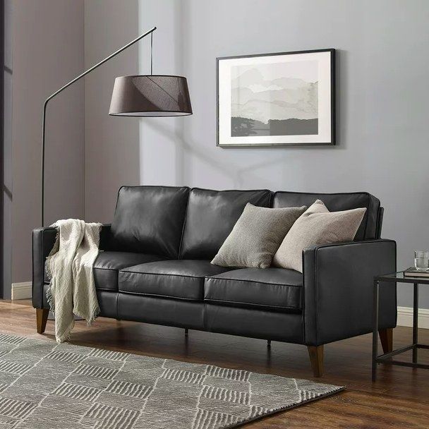 A black sofa adorned with throw pillows and a blanket in a modern gray living room.