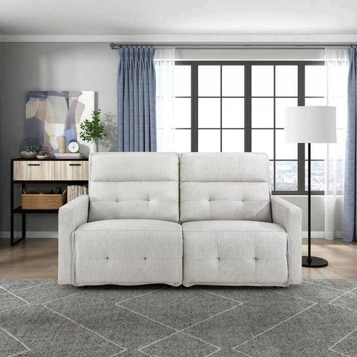 A stylish modern living room featuring a light-colored tufted loveseat, a floor lamp, a console table, and a large window that brings in natural light.