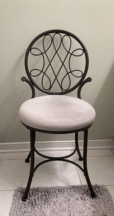 Reviewer image showcasing a black metal chair with a white fabric seat and swirling loops at the back, placed atop a bathroom tile and carpeted floor.