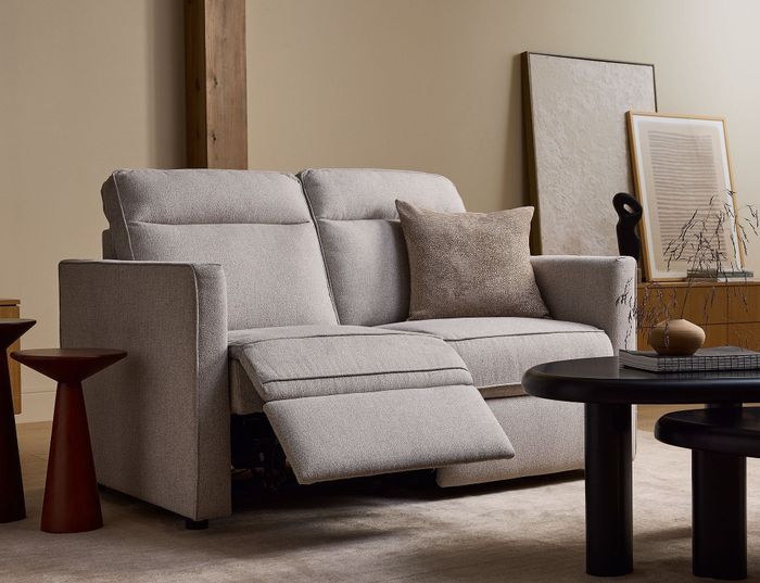 A reclining grey sofa in a contemporary living room featuring sleek decor, a black coffee table, artistic pieces, and a small side table, perfect for relaxing after a day of shopping