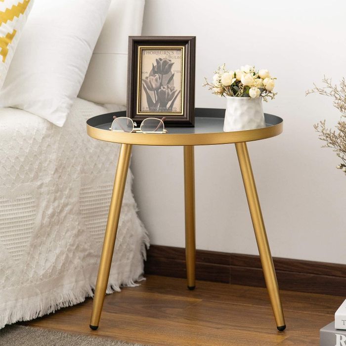 The circular gold-toned table holds a small flower pot, glasses, and a photo frame.