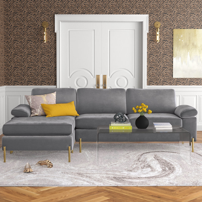 A trendy living room featuring a gray sectional sofa, a glass coffee table, stylish pillows, and a modern abstract painting on the wall.