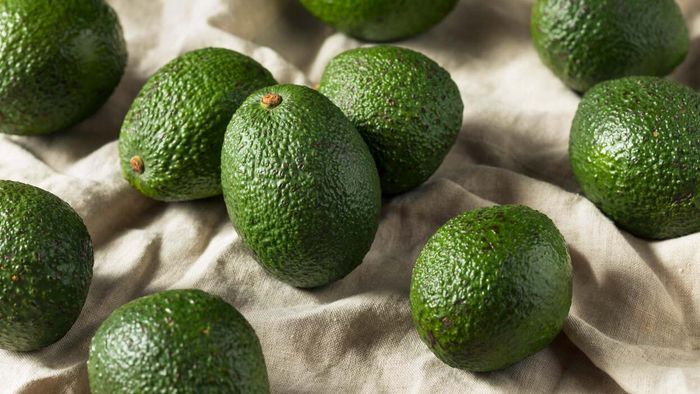 Green avocados scattered across a beige tablecloth.