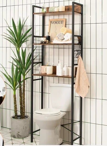 A bathroom with a contemporary over-the-toilet storage rack displaying towels, decor, and toiletries.