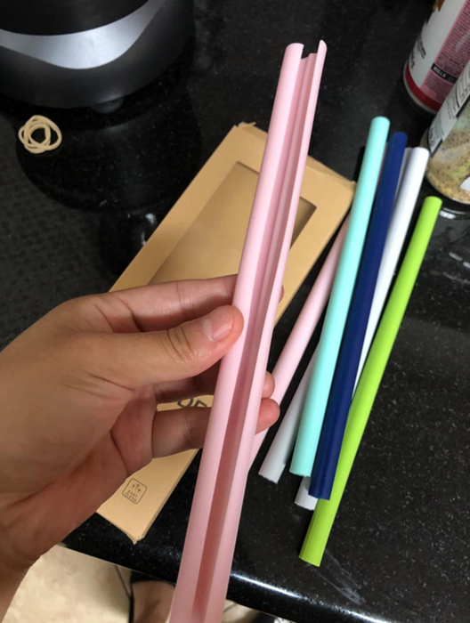 A reviewer holding a set of multicolored straws, showing a pink one horizontally to reveal the inside.