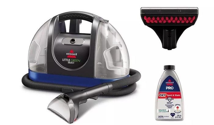 A Bissell Little Green portable carpet cleaner, complete with a hose and attachment, a bottle of cleaning solution, and an additional brush attachment.