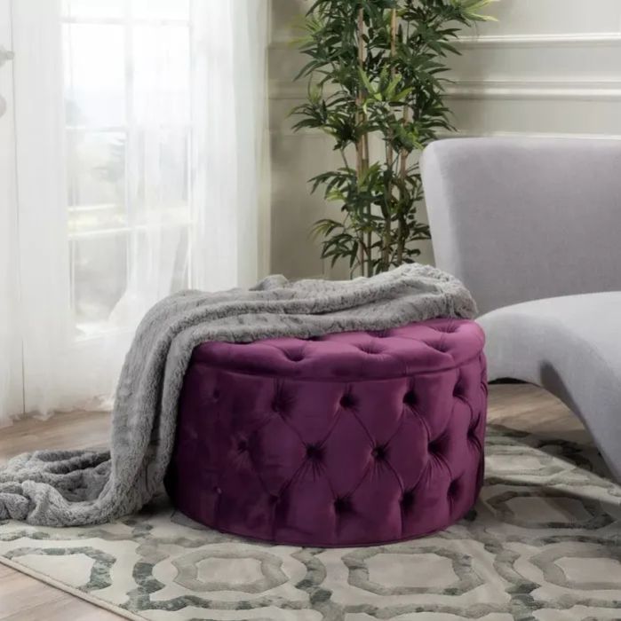 The plum-colored ottoman with a cozy blanket draped over it