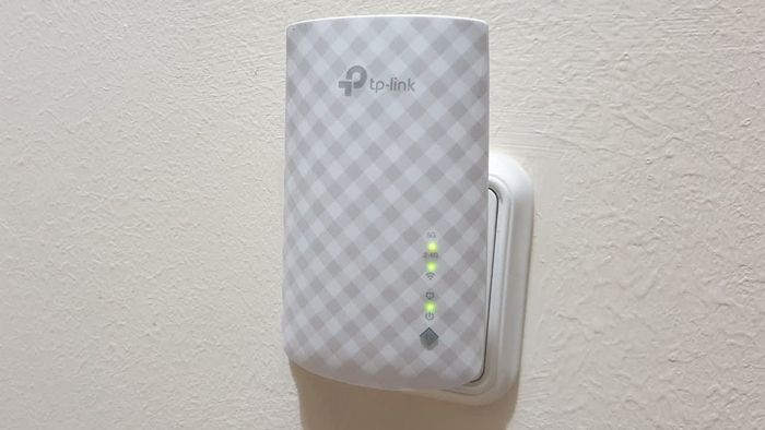 TP-Link range extender plugged into a wall socket, with signal strength indicator lights showing active connectivity